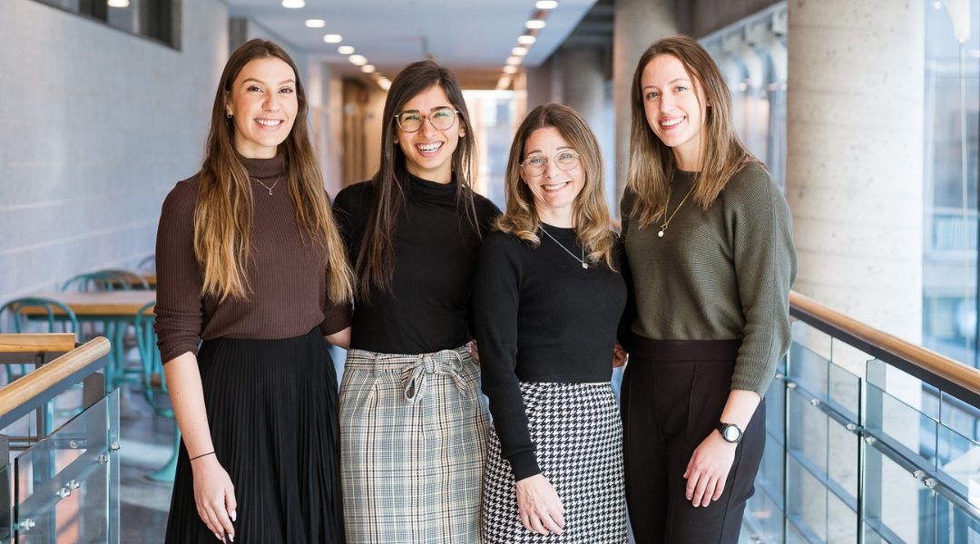 Four registered dietitians from TeamNutrition in professional attire standing in a modern hallway with large windows