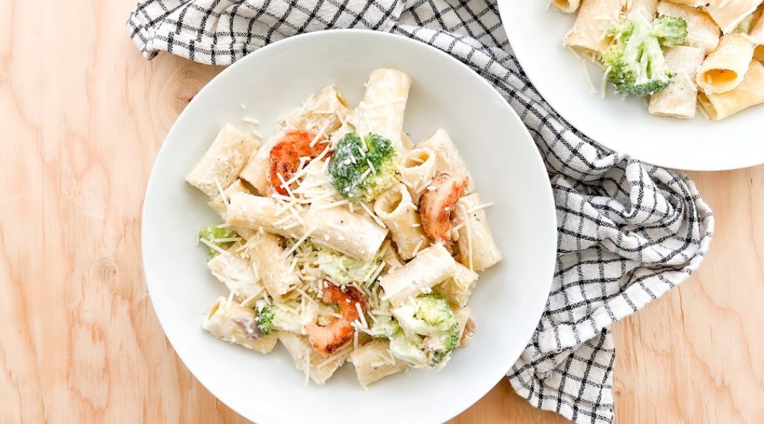 Rigatoni pasta with creamy Alfredo sauce, shrimp, and broccoli, garnished with Parmesan cheese on a white plate.