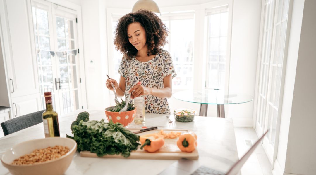 Woman preparing a salad with fresh vegetables in a bright kitchen, highlighting healthy and simple eating.