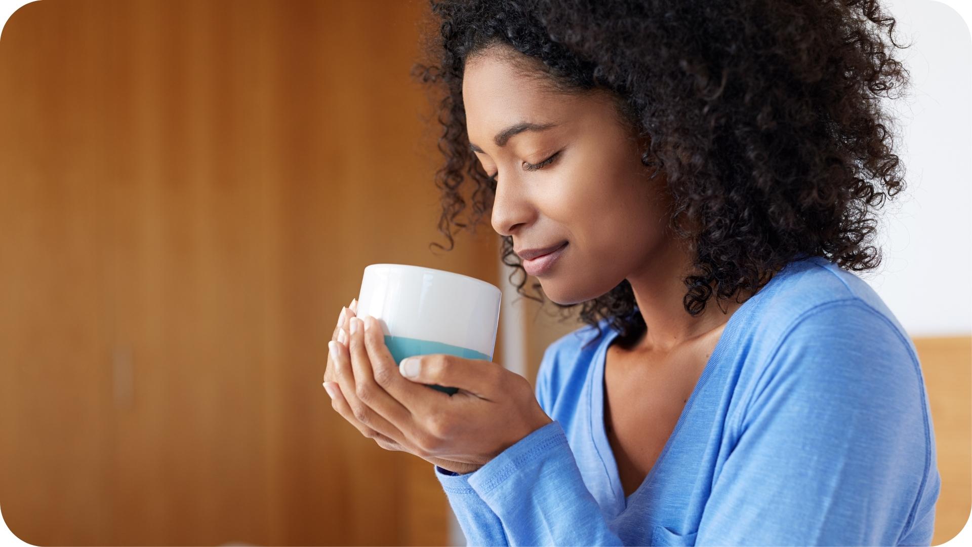 Woman enjoying a hot drink, eyes closed, holding a white cup