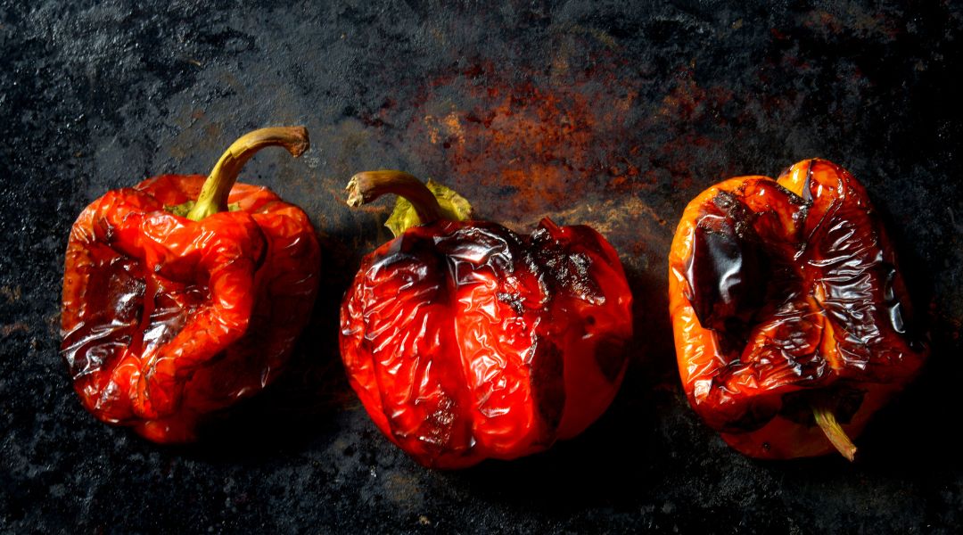 Three roasted red bell peppers with charred skin on a dark, rustic background