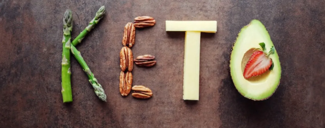 Keto written on a wooden background with vegetables and proteins