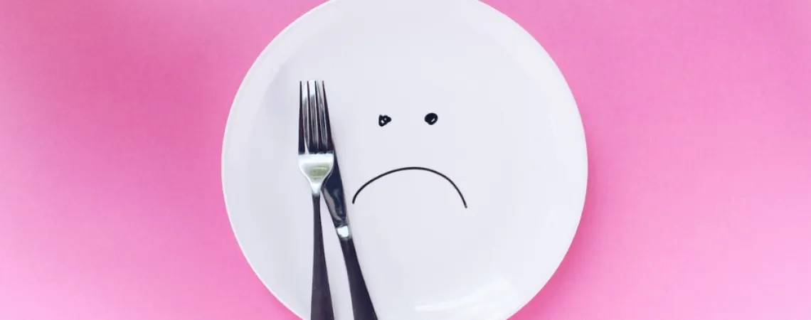 sad plate with a fork and a knife on a pink background