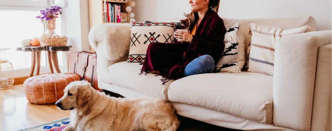 Femme assise sur un canapé avec une tasse, un chien couché sur un tapis coloré devant elle - Woman sitting on a couch with a cup, a dog lying on a colorful rug in front of her