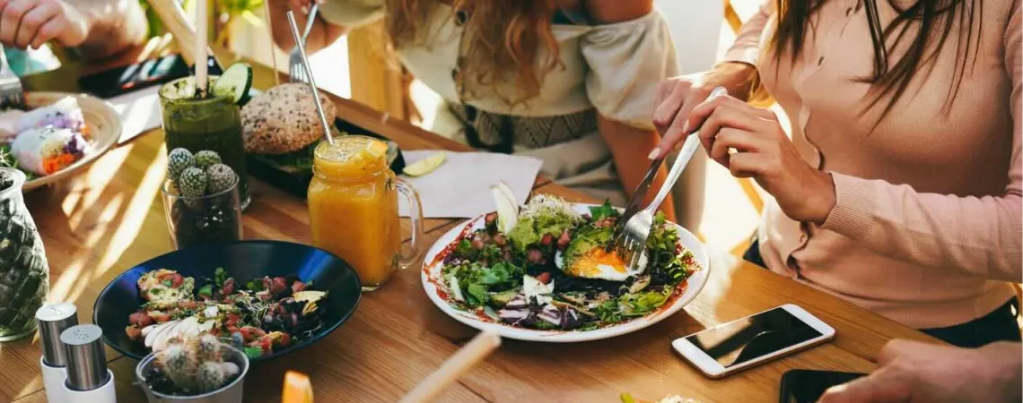Group of people enjoying a meal with fresh salads, smoothies, and bread at an outdoor table.