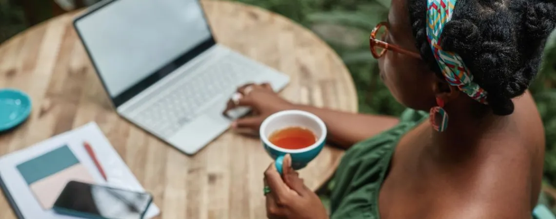 A woman drinking her hot tea while working outside in front of her computer.