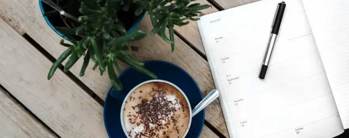 A coffee, agenda and a plant on a wood table