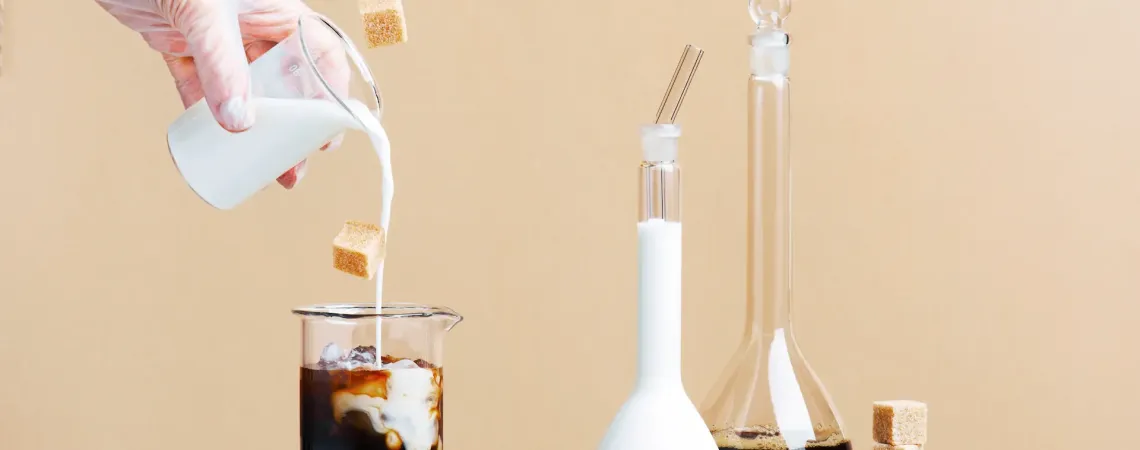 Main versant du lait dans un café glacé avec des morceaux de sucre flottants - Hand pouring milk into iced coffee with floating sugar cubes