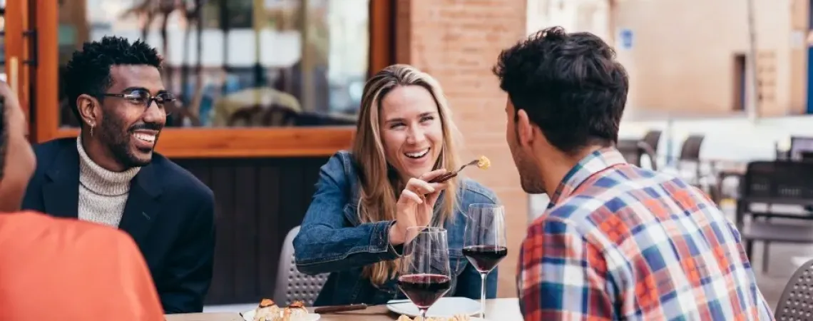 Group of friends enjoying a meal together at an outdoor restaurant, sharing laughs and conversation. The setting reflects a casual and joyful dining experience, highlighting the social benefits of eating out while maintaining healthy choices.