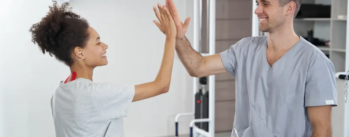 Physiothérapeute sourit et fait un high five avec une jeune femme - A physiotherapist smiles and gives a high five to a young woman