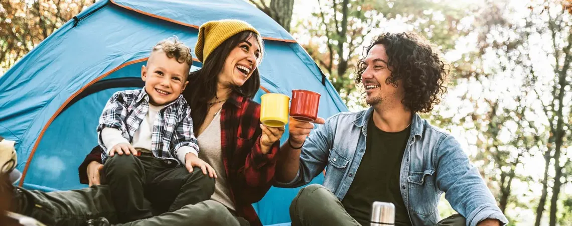 A happy family camping in the forest, drinking tea in front of their tent - Une famille heureuse campe dans la forêt, buvant du thé devant leur tente