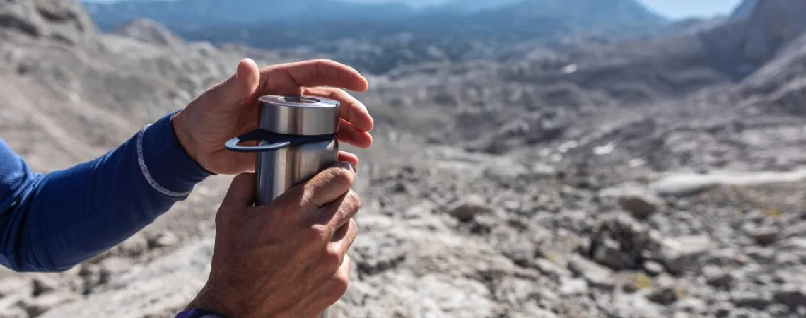 Mains ouvrant une bouteille d'eau en montagne.