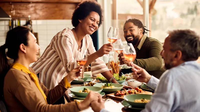 Groupe d'amis multiculturels trinquant avec des verres de vin rosé autour d'un repas - Multicultural group of friends toasting with glasses of rosé wine around a meal
