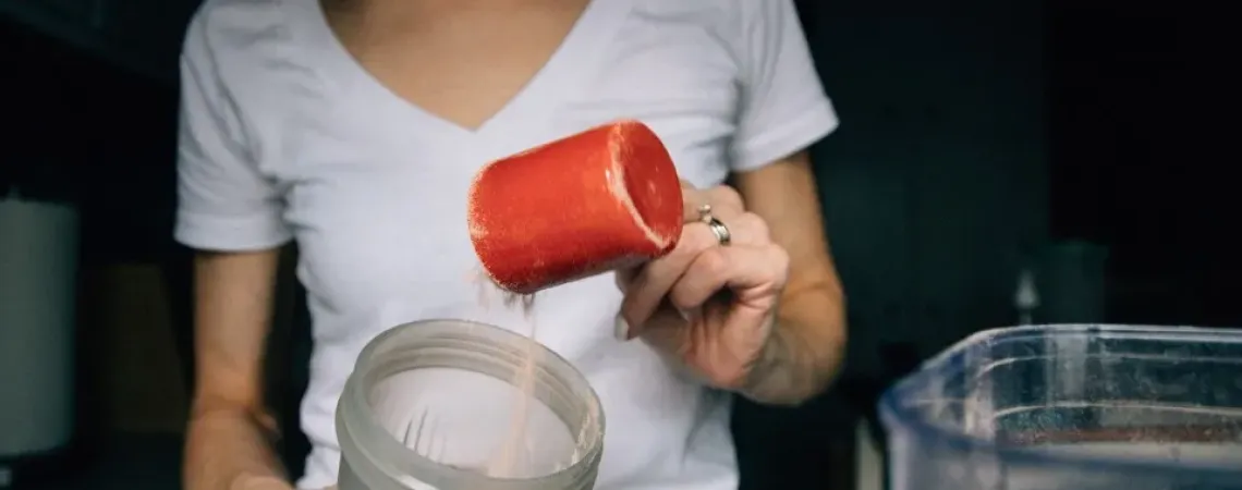 A woman putting a cup of protein powder in the blender