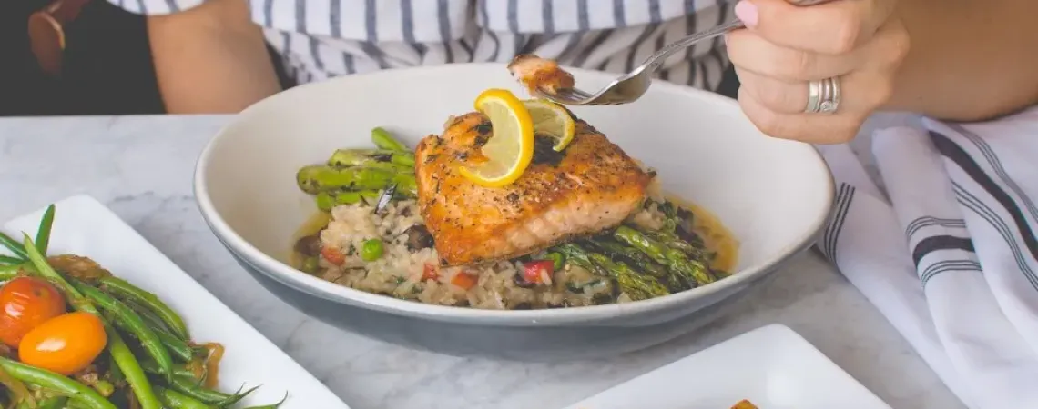 Woman eating salmon served on a bed of asparagus and rice