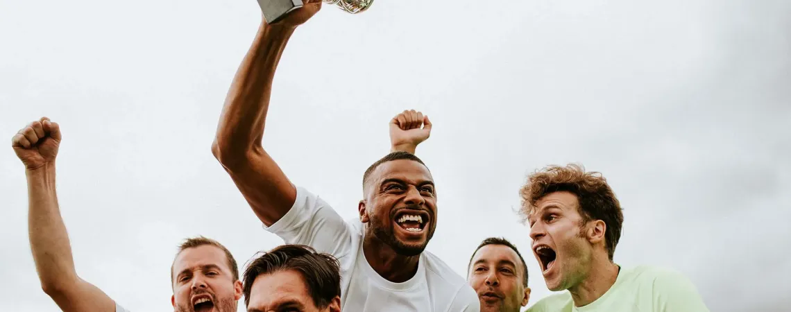 Group of excited men in white jerseys celebrating victory as one holds up a trophy - Groupe d'hommes enthousiastes en maillots blancs célébrant leur victoire, l'un d'eux brandissant un trophée