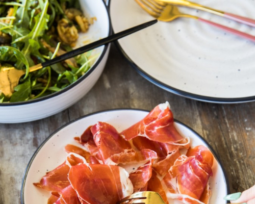 A plate of prosciutto and a plate of arugula