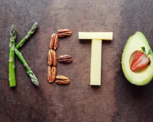 Keto written on a wooden background with vegetables and proteins