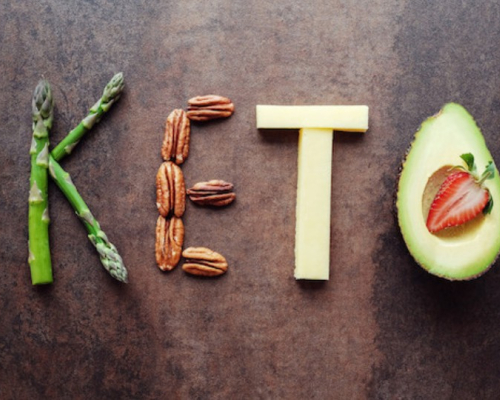 Keto written on a wooden background with vegetables and proteins