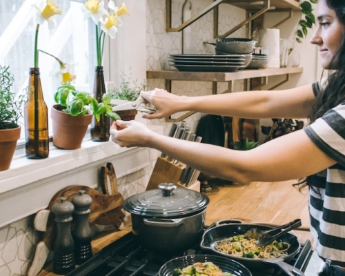 woman in a kitchen cooking a dish and adding basil