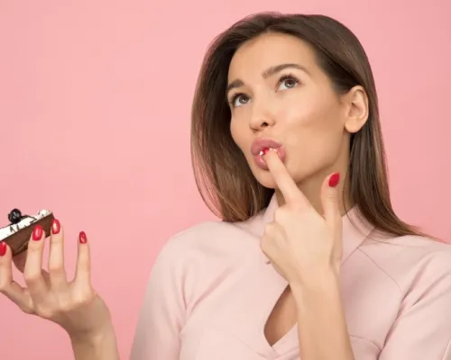 Woman eating a cake in front of a pink screen