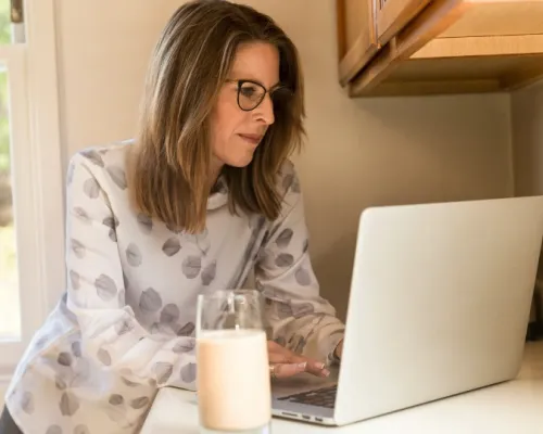 menopausal woman in front of a computer with a glass of milk