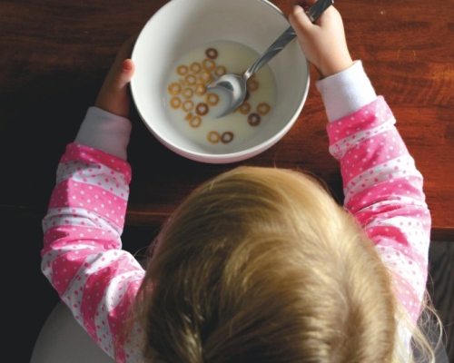 Child with a pink shirt eating cereals with milk