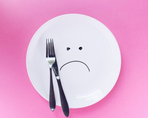 sad plate with a fork and a knife on a pink background