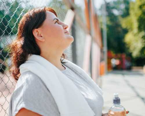 Woman taking a break after outdoor exercise, holding a water bottle, symbolizing a weight loss journey