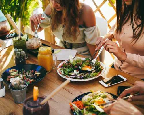 Group of people enjoying a meal with fresh salads, smoothies, and bread at an outdoor table.