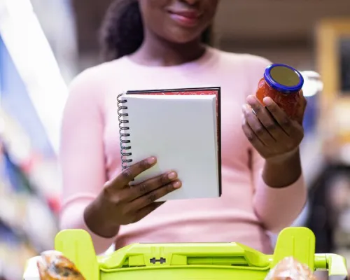 Personne tenant un carnet et un pot de sauce tomate à l'épicerie - Person holding a notebook and a jar of tomato sauce in a supermarket