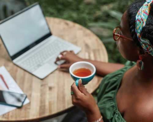 A woman drinking her hot tea while working outside in front of her computer.