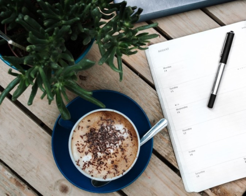 A coffee, agenda and a plant on a wood table