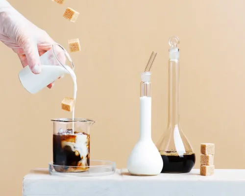Main versant du lait dans un café glacé avec des morceaux de sucre flottants - Hand pouring milk into iced coffee with floating sugar cubes
