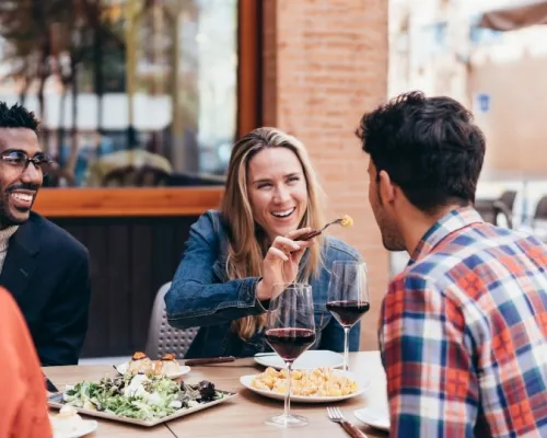 Group of friends enjoying a meal together at an outdoor restaurant, sharing laughs and conversation. The setting reflects a casual and joyful dining experience, highlighting the social benefits of eating out while maintaining healthy choices.