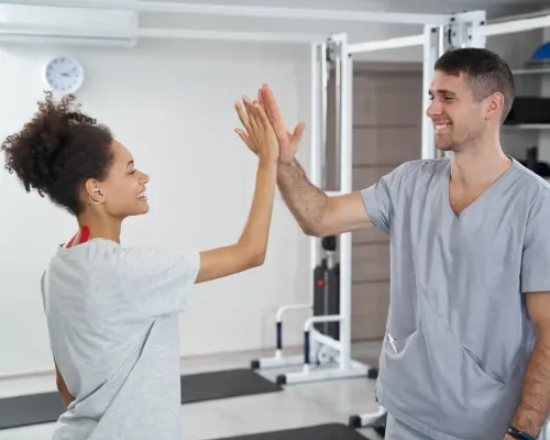 Physiothérapeute sourit et fait un high five avec une jeune femme - A physiotherapist smiles and gives a high five to a young woman