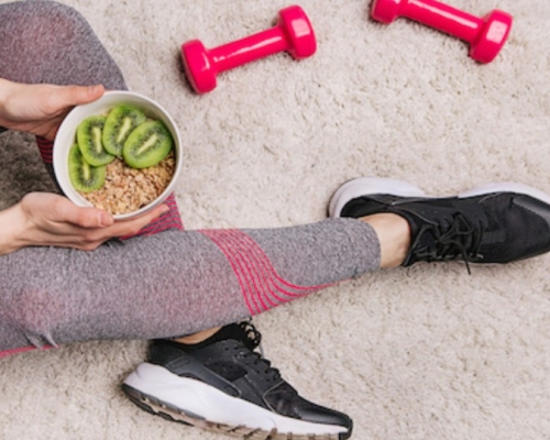 femme assise avec un bol de kiwis et deux altères rouges