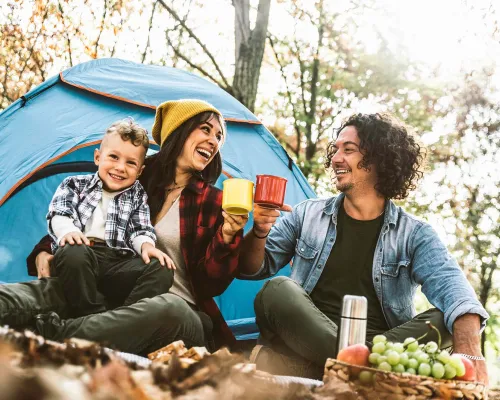 A happy family camping in the forest, drinking tea in front of their tent - Une famille heureuse campe dans la forêt, buvant du thé devant leur tente