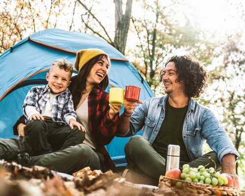 A happy family camping in the forest, drinking tea in front of their tent - Une famille heureuse campe dans la forêt, buvant du thé devant leur tente
