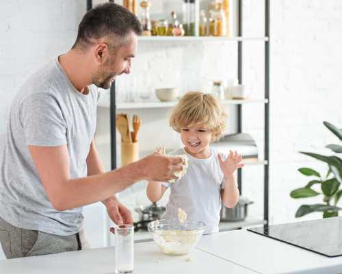 Un père et son fils rient et s'amusent en préparant de la pâte dans une cuisine moderne et lumineuse - A father and his son are laughing and having fun while making dough in a bright, modern kitchen