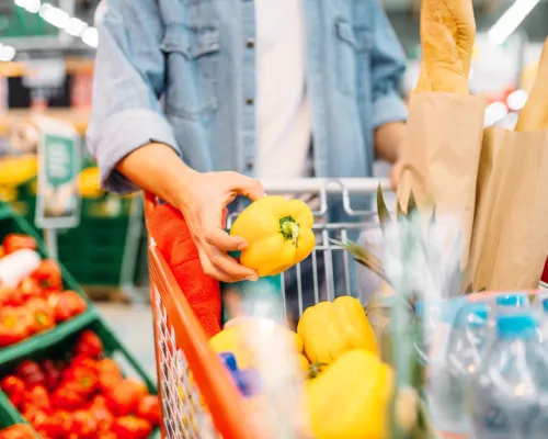 A shopper selects a yellow pepper from a display of fresh produce at the grocery store.