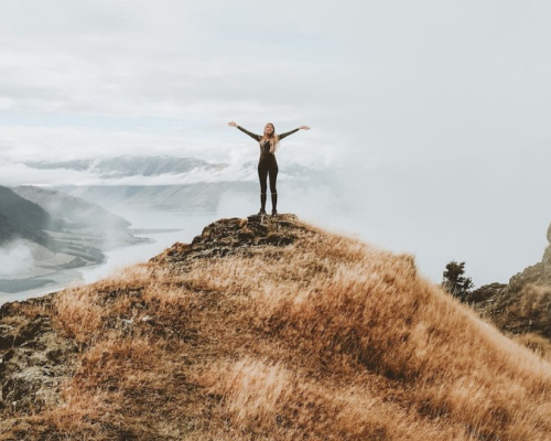 Une femme avec les bras en croix au sommet d'une montagne.