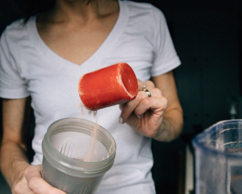 A woman putting a cup of protein powder in the blender