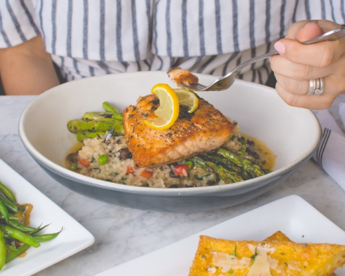 Woman eating salmon served on a bed of asparagus and rice 