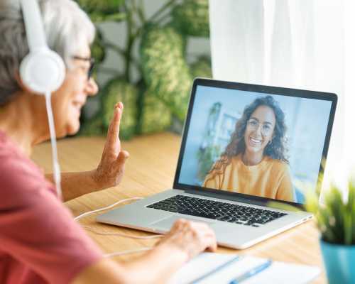 Older woman with headphones waving during a video call - Femme âgée avec des écouteurs faisant signe de la main pendant un appel vidéo