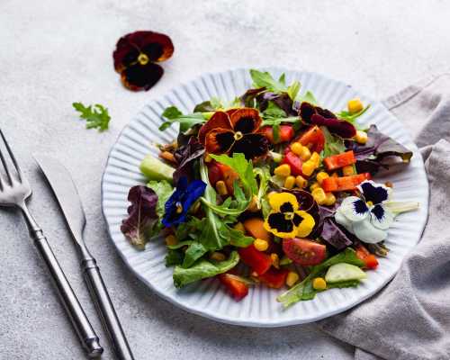 Une salade colorée garnie de fleurs comestibles, avec des légumes variés et des pensées violettes, jaunes et blanches - A colourful salad garnished with edible flowers, featuring various vegetables and purple, yellow, and white pansies