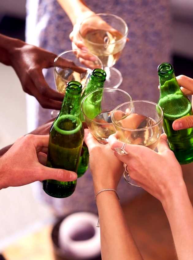 Un groupe de mains diverses trinquant avec des bouteilles de bière verte et des verres de vin dans une ambiance festive. A group of diverse hands toasting with green beer bottles and wine glasses in a celebratory setting.