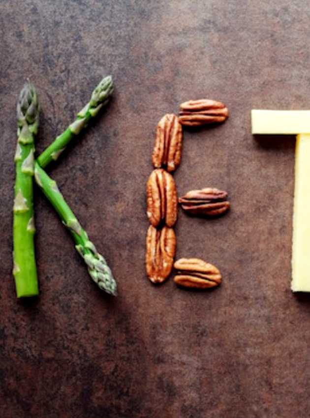 Keto written on a wooden background with vegetables and proteins