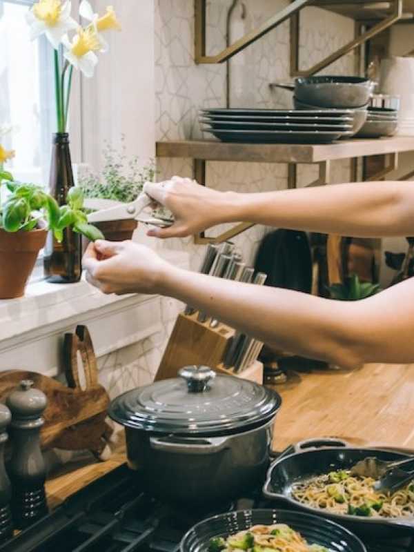 woman in a kitchen cooking a dish and adding basil