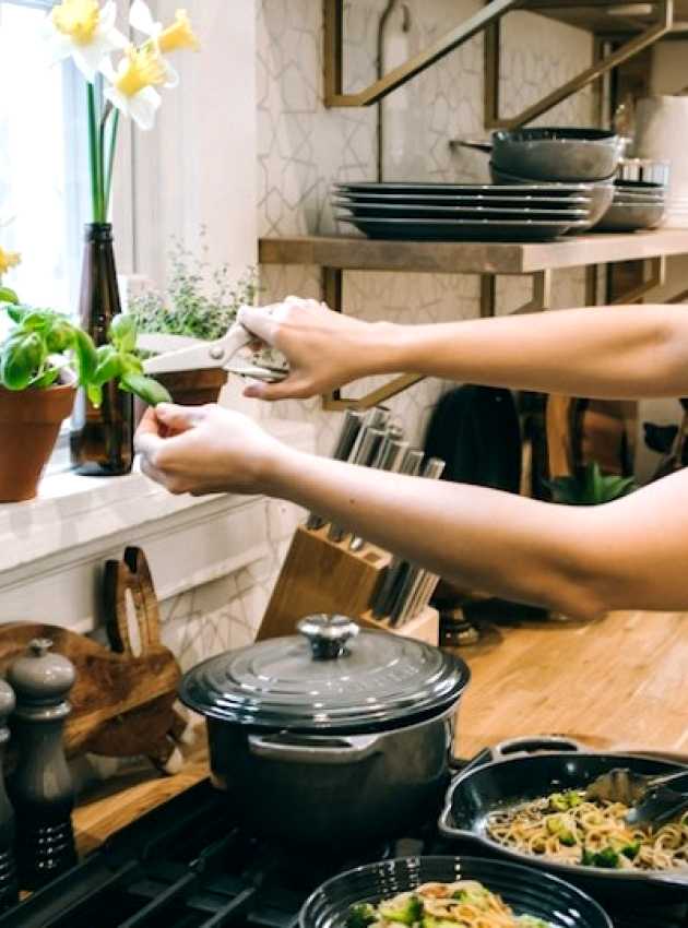 woman in a kitchen cooking a dish and adding basil